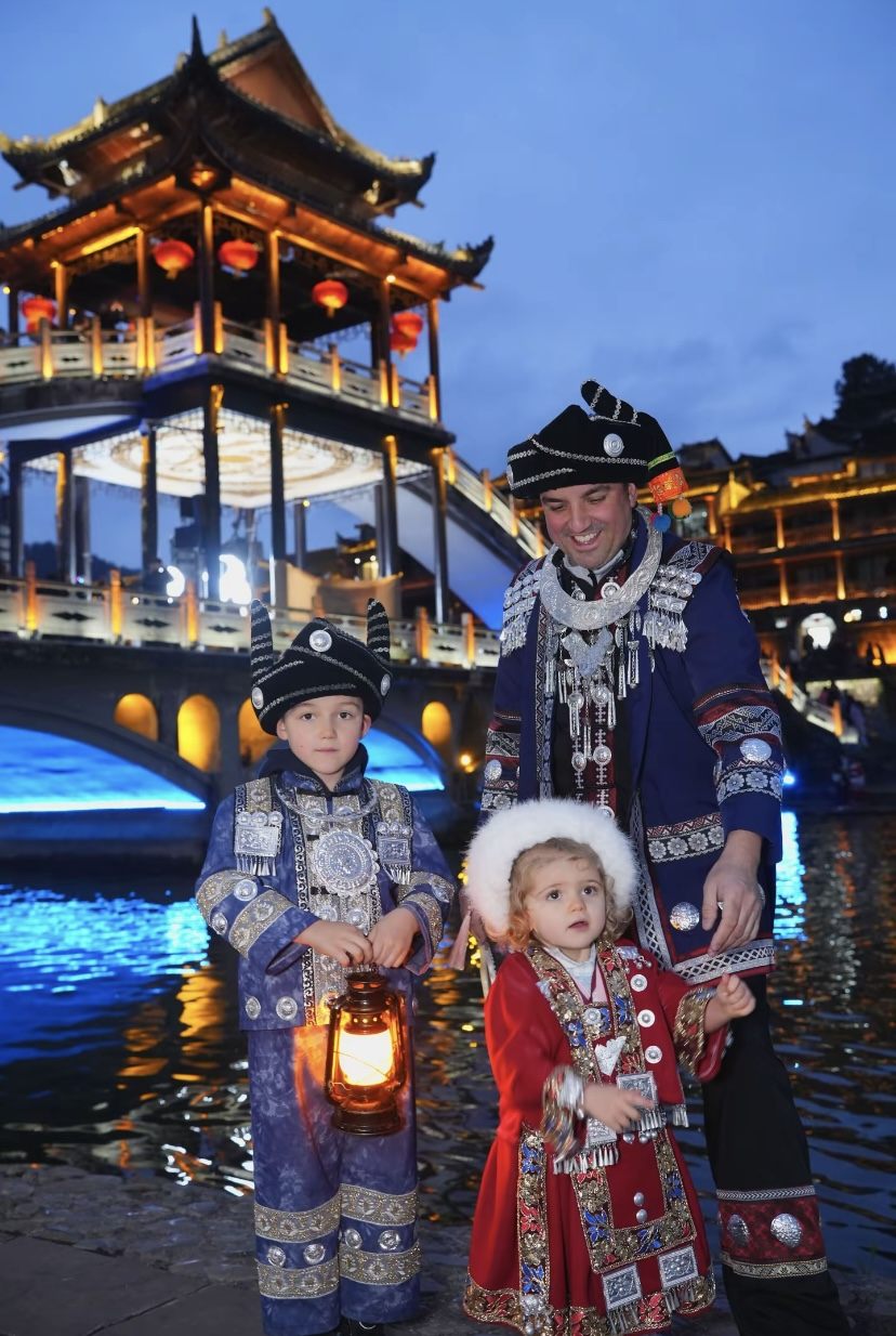 A family in Miao ethnic costume by the lantern-lit bridge in Fenghuang on a private family tour