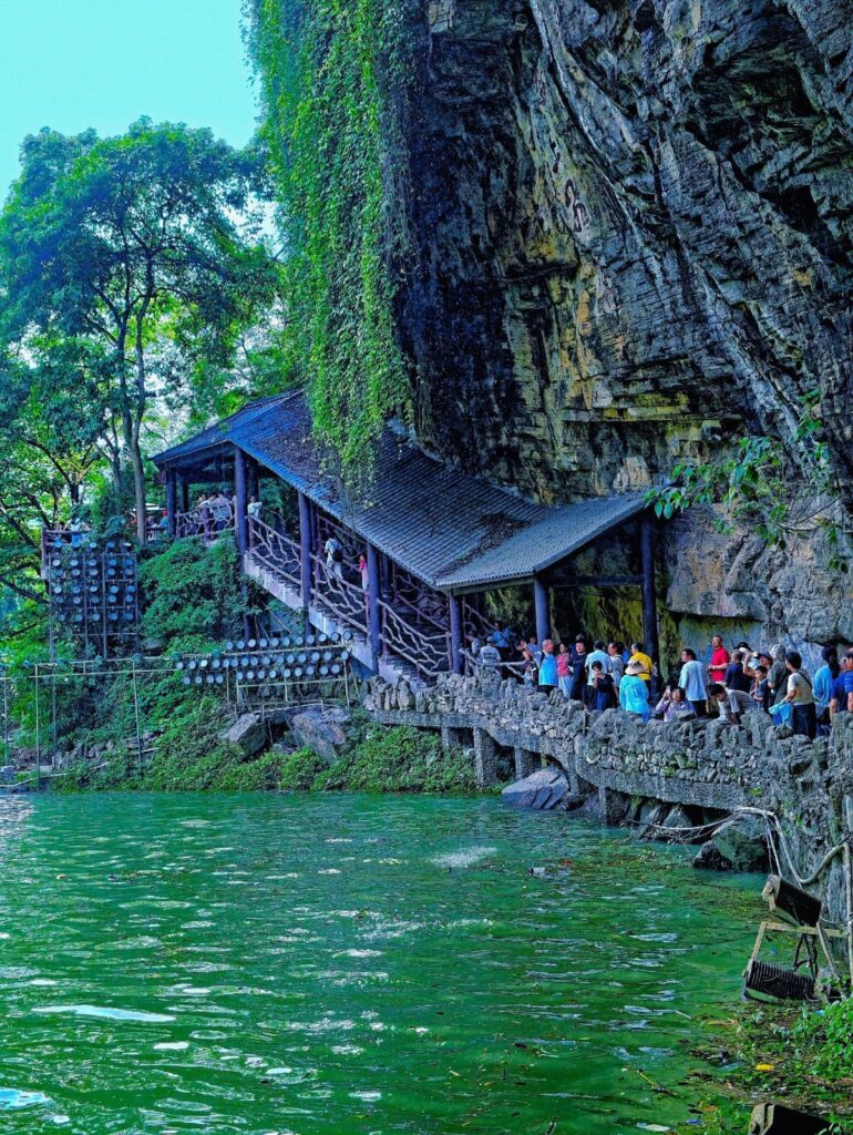 Covered walkway and viewing path at the base of the Furong Ancient Town waterfall, busy with visitors