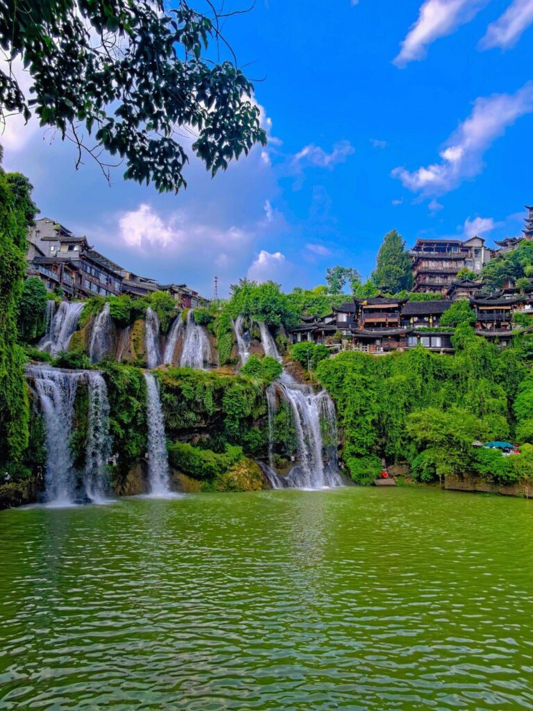 Furong Ancient Town waterfall with Tujia stilt houses on the cliff above, Hunan, daytime