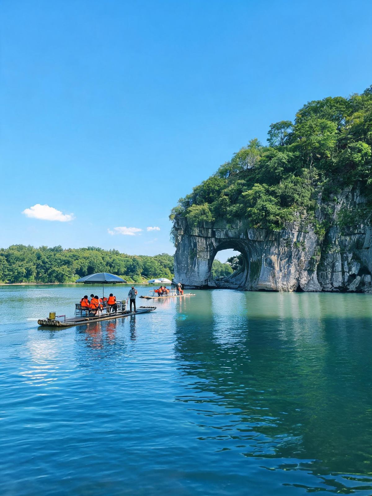 Elephant Trunk Hill in Guilin, a limestone arch over the Li River, with a bamboo raft of visitors in life jackets on the water