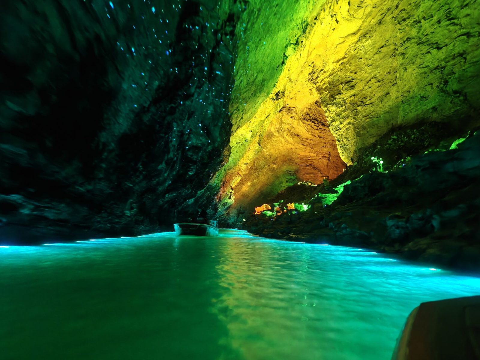 A boat on the underground Xiangshui River in Huanglong Cave, Zhangjiajie, with the rock lit green and yellow above the water