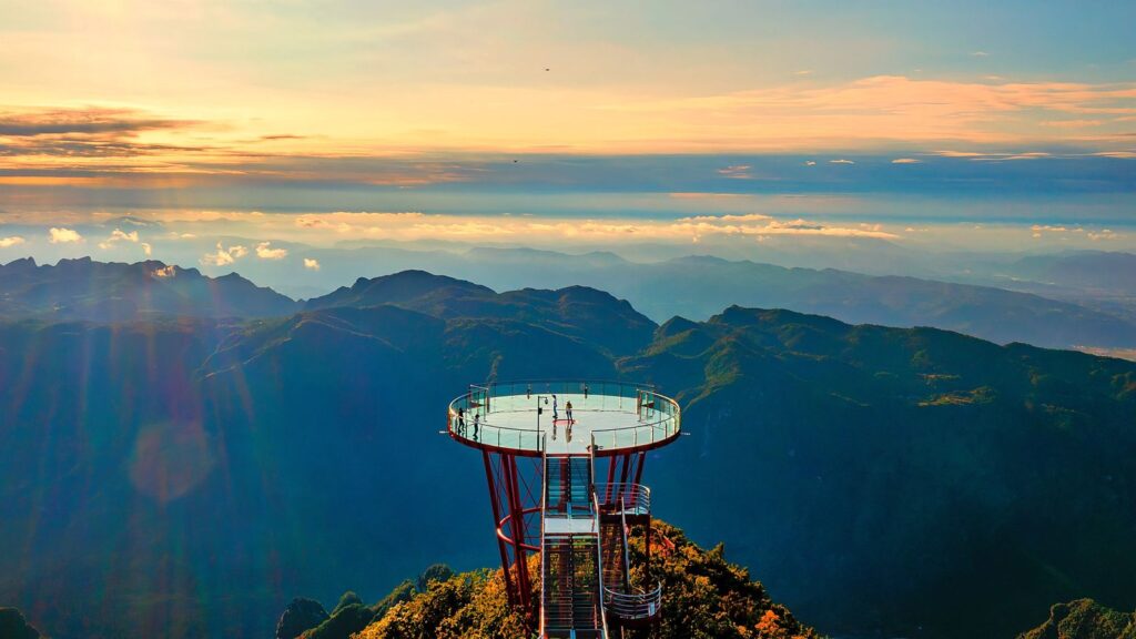 The 1520 Eye of Sky glass viewing platform on Qixing Mountain, Zhangjiajie, projecting from the cliff at sunset with mountain ridges beyond