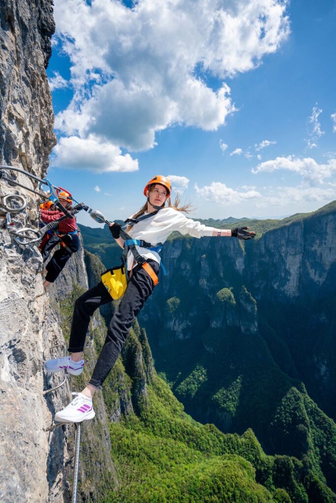 A climber leaning out from the cliff on the Qixing Mountain via ferrata, held by two lanyards clipped to the safety cable, Zhangjiajie