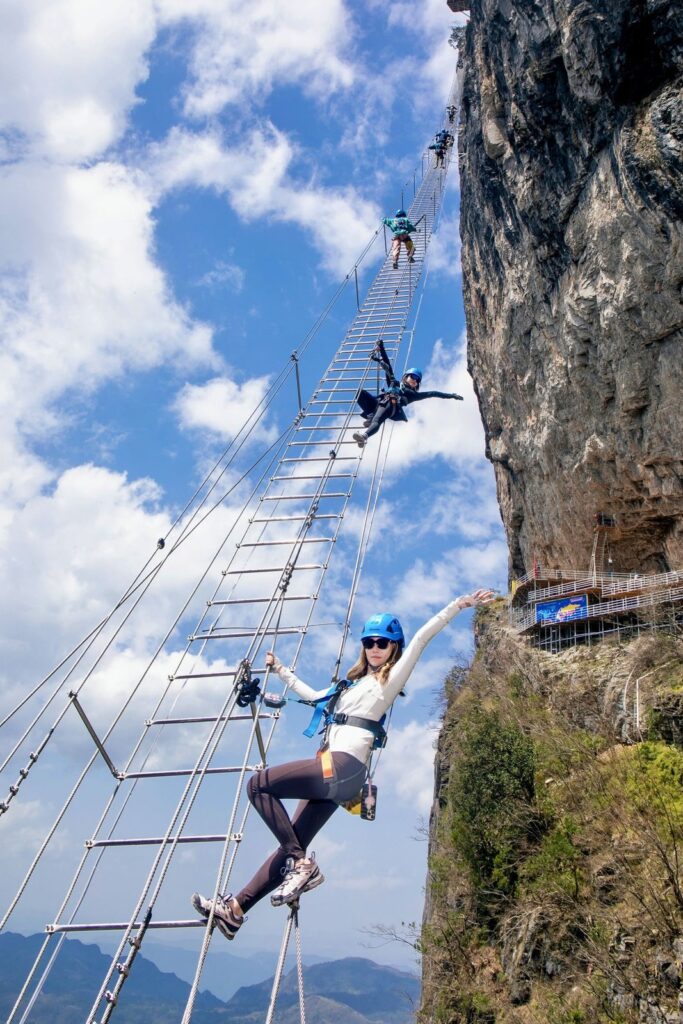 A climber on a rock ledge of the Qixing Mountain via ferrata, Zhangjiajie, with limestone cliffs and forested valleys behind
