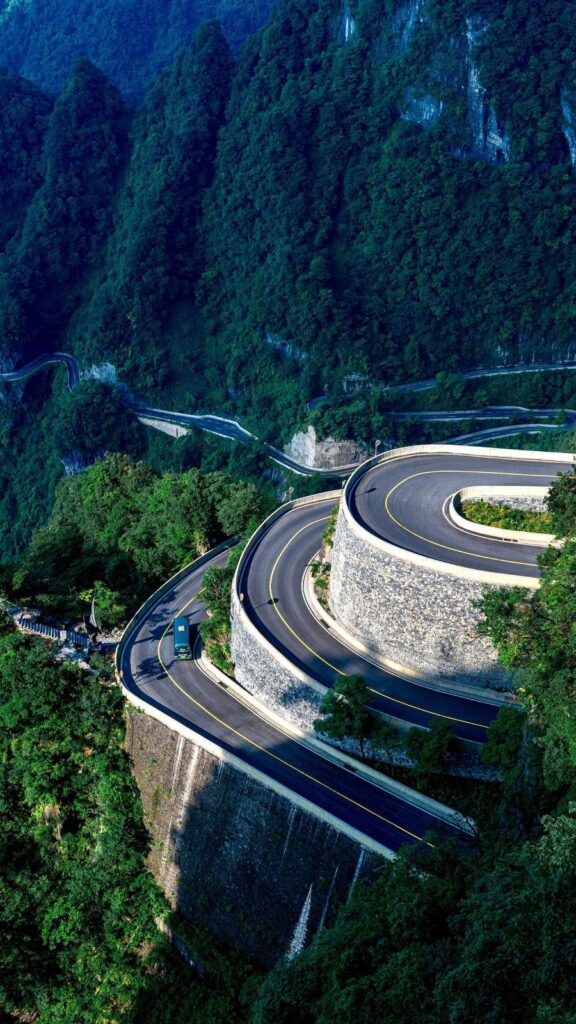 Shuttle bus rounding a stone-walled hairpin on the 99-bend road up Tianmen Mountain, more bends visible below