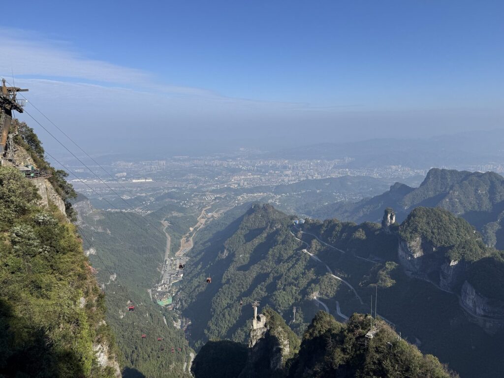 The 99-bend road and the main cableway seen from the summit of Tianmen Mountain, with Zhangjiajie city on the plain beyond