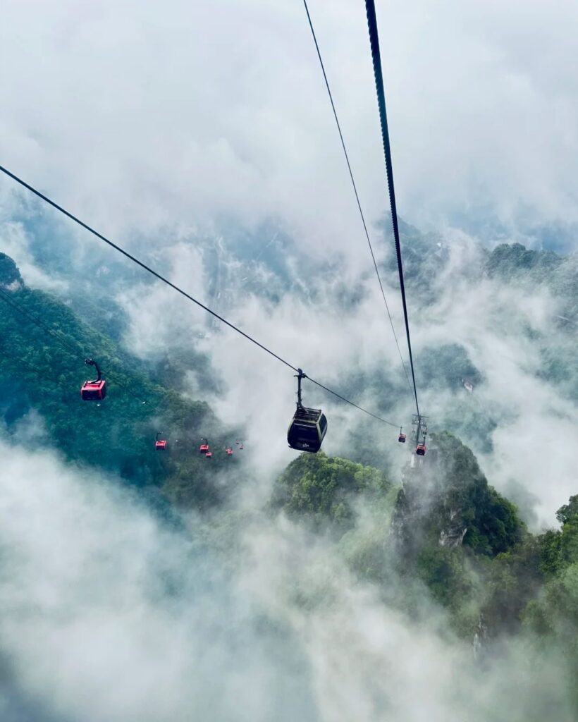 Cable cars of Tianmen Mountain disappearing into cloud above forested peaks