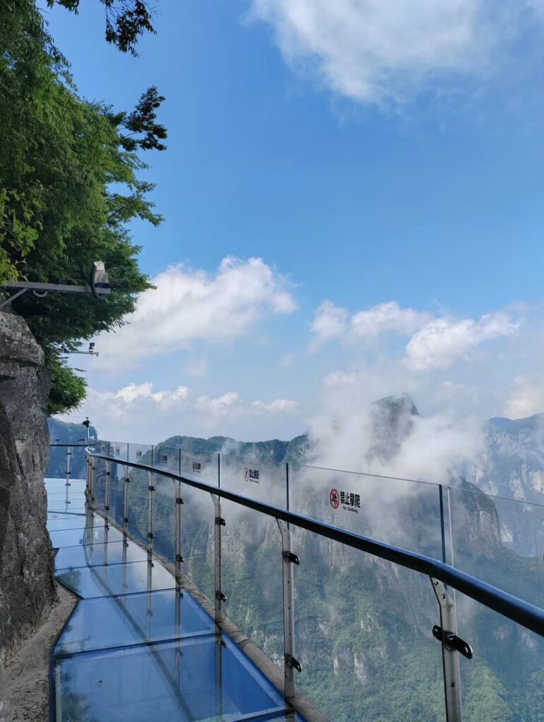 Glass walkway on the cliff face of Tianmen Mountain with clouds drifting past the railings