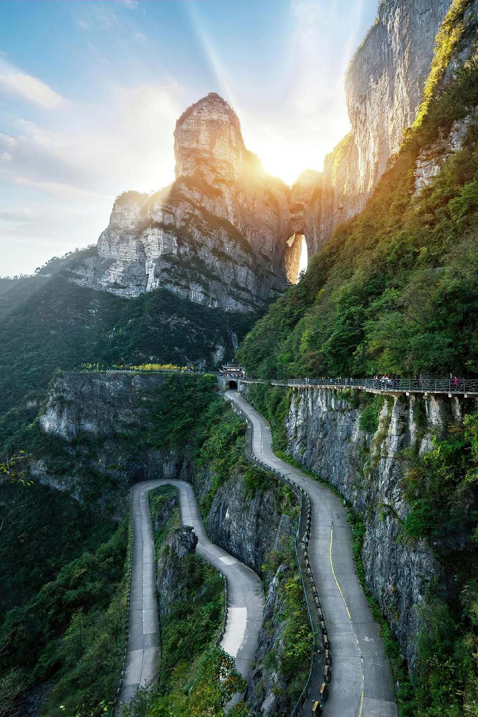 Tianmen Mountain, Zhangjiajie: sunlight through Heaven’s Gate above the 99-bend Tongtian Avenue, cliffside walkway on the right