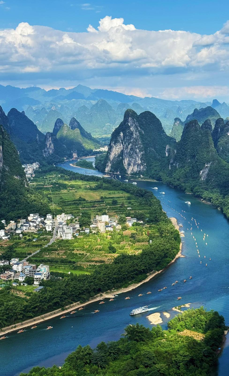 The Li River bending between green karst peaks seen from Xianggong Mountain near Xingping, Guilin, with cruise boats and a riverside village