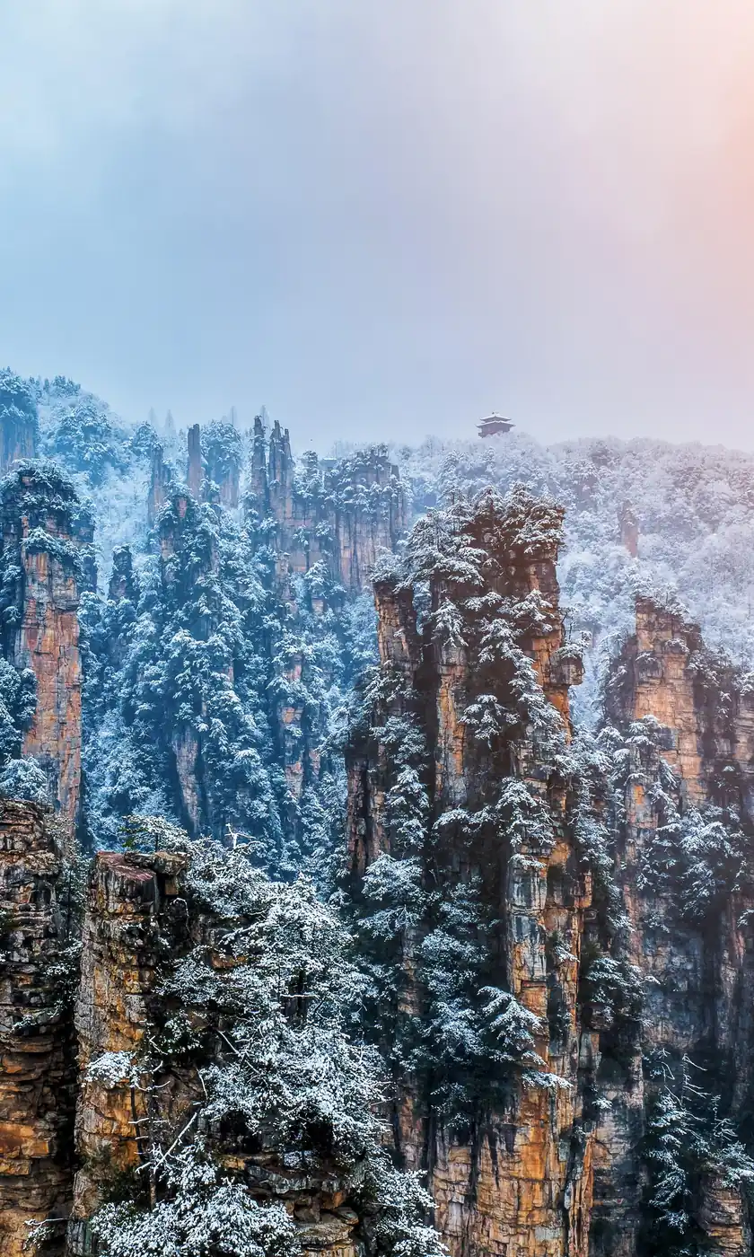 Snow on the sandstone pillars of Tianzi Mountain, Zhangjiajie, with a pavilion on the ridge after a winter snowfall